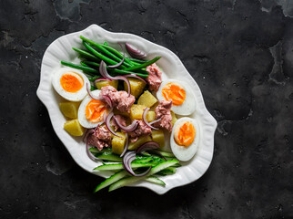 Breakfast, appetizers, snack plate - boiled eggs, potatoes, string beans, red onion, cucumber, canned tuna salad on a dark background, top view