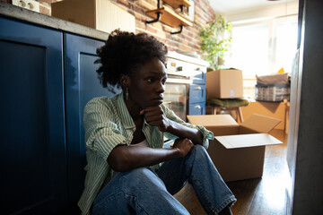 Woman sitting on the floor at home looking thoughtful with moving boxes around