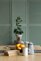 Citruses with teapot, books and vase on dining table in room