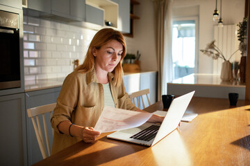 Concerned woman holding bill using laptop at home