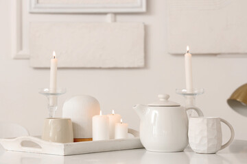 Fototapeta na wymiar White teapot with cup and burning candles on dining table in light room
