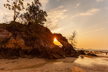amazing The evening sun shone through the large rock hole and sparkled beautifully. .stunning sunset in the hole of unusual rock wave eroded into .the cavity like the arch with a hole.. - obrazy, fototapety, plakaty