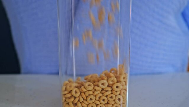 Caucasian Female Pouring In Tasty Sweet Honey Cereal Rings into Translucent Glass Container