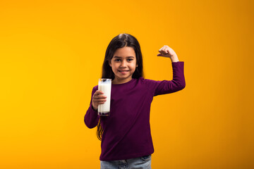Smiling child girl holding glass of milk and showing strenght gesture. Nutrition and health concept