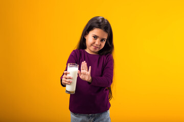 Kid girl with dairy allergy showing stop gesture front glass of milk on yellow background. Lactose...