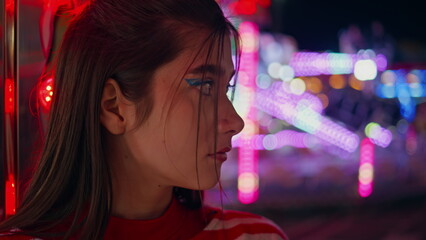 Fototapeta premium Attractive girl rest funfair closeup. Unhappy sad woman at neon amusement park