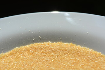 Food, cooking homemade meals. Small yellow grains of gelatin are placed on a white glass plate and illuminated by sunlight. 