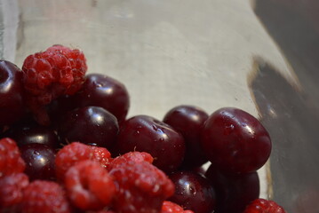 Produce, fresh fruits, red homemade raspberries, cherries arranged in a glass jar.