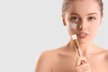 Young woman with facial mask and brush on light background, closeup