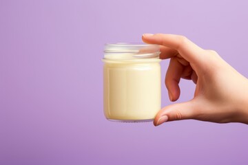 Close-up photo of a devious hand reaching for a jar of mayonnaise cleverly disguised as vanilla pudding for an April Fools' Day gag, against a solid pastel lavender backdrop - obrazy, fototapety, plakaty