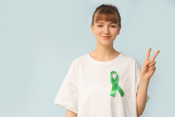 Young woman with green ribbon showing victory gesture on light background. Glaucoma awareness month