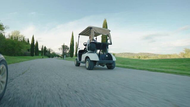 Bottom view shot of driving golf carts along the pavement road of large golf course in the countryside, luxury sport of adrenaline and experience, cars delivering players to the place of game. Golf