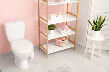 Fototapeta na wymiar Interior of stylish bathroom with houseplant and ceramic toilet bowl near pink wall