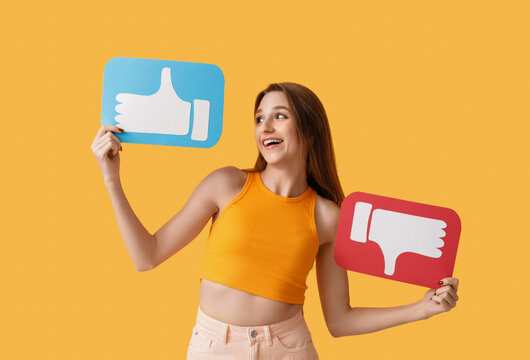 Pretty young woman holding like and dislike icons on orange background