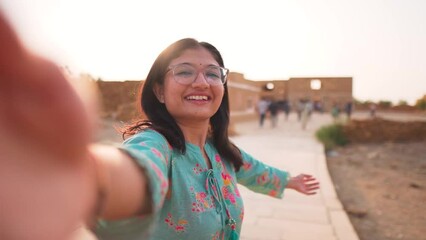 Selfie video of cheerful young Indian blogger girl smiling at camera while standing at Kuldhara village near Jaisalmer in Rajasthan, India. Social media travel influencer making video.