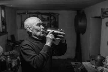 old man drinks wine from a glass bottle in the dark basement