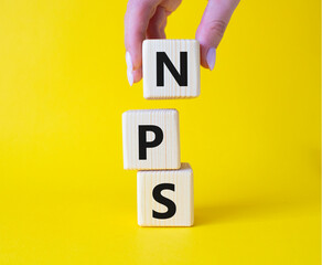 NPS - Net Promoter Score symbol. Wooden cubes with words NPS. Businessman hand. Beautiful yellow...