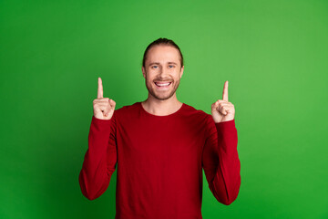 Photo of satisfied toothy beaming man with stubble dressed red pullover indicating at offer empty...