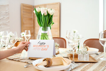 Female hand with stylish table setting and greeting card for International Women's Day celebration