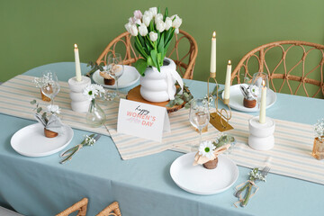 Beautiful table setting with burning candles and tulip flowers for International Women's Day celebration near green wall