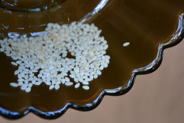 Healthy foods, seeds and grains. Small white sesame seeds placed on a dark, black, transparent glass plate.