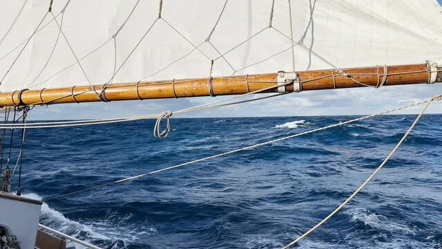 view from a retro style sailing schooner during the passage of the Drake Strait, wooden boat boom, lots of ropes, large waves of the southern ocean in sunny weather