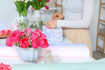Obraz na płótnie Canvas Woman packing gift box for International Women's Day at light table with beautiful flowers