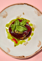 Top view of beetroot mille-feuille with pesto sauce on an elegant plate, presented on a soft pink background
