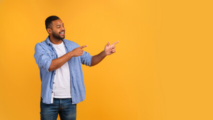 Energetic young black man pointing at copy space with two hands