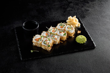 Bonito roll with tuna flakes and salmon inside, served on a black slate with soy sauce, wasabi, and ginger