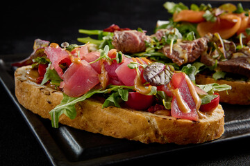 Gourmet bruschetta set with salmon, roast beef, and tuna on a black plate, side angle view