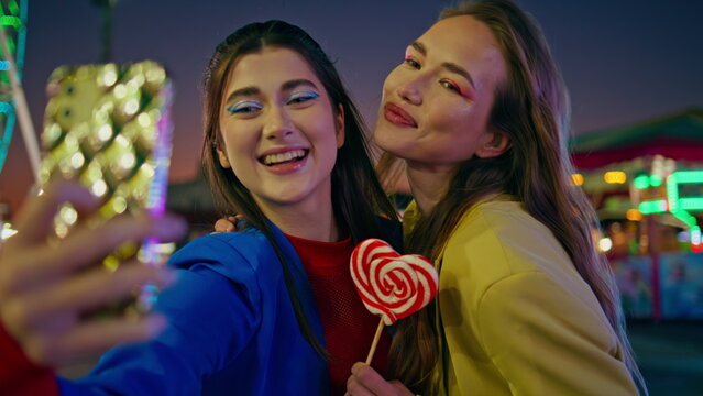 Joyful friends making selfie at night luna park closeup. Happy girls having fun