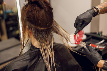 Close up of colorist dyes hair of woman with brush and foil in beauty salon