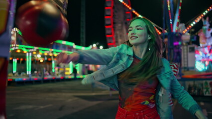 Smiling girl hitting boxing machine at amusement park. Cheerful teenagers having
