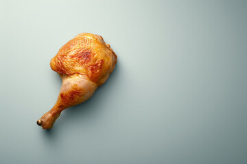 Fried or baked chicken leg with golden skin isolated on light blue background with space for text or inscriptions, minimalist scene top view
