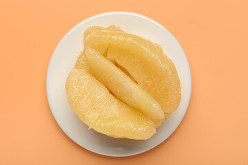 Plate with ripe pomelo pieces on orange background