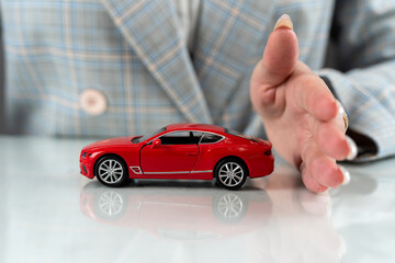 Small toy red car in female hands as insurance