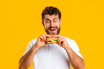 Funny hungry bearded man looks at burger with temptation, studio