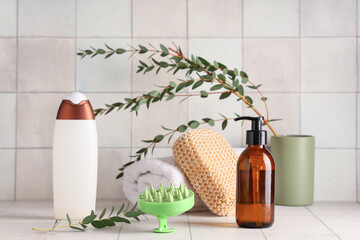 Fototapeta na wymiar Silicone head massage brush with bottles of cosmetic products, bath sponge and eucalyptus on white tile background