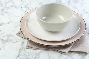 Clean plates, bowl and napkin on white marble table, closeup. Space for text