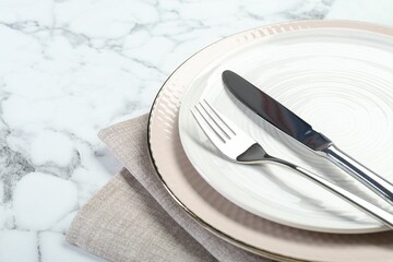 Clean plates, cutlery and napkin on white marble table, closeup. Space for text