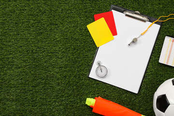 Soccer ball and different referee equipment on green grass, flat lay. Space for text