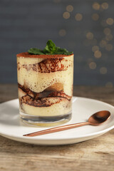 Tasty tiramisu and mint in glass on wooden table, closeup