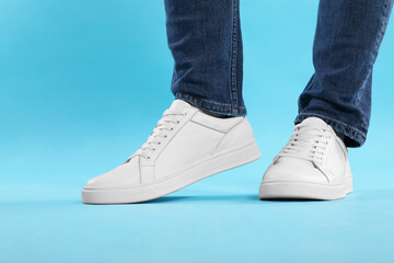 Man wearing stylish white sneakers on light blue background, closeup