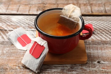 Tea bags and cup of aromatic drink on wooden rustic table, closeup