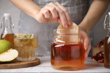 Woman putting Scoby fungus into jar with kombucha at white wooden table, closeup