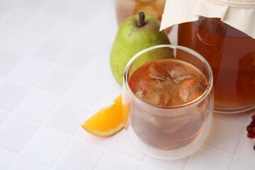 Tasty kombucha with ice cubes and fresh fruits on white tiled table, space for text