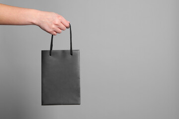 Woman holding paper shopping bag on grey background, closeup. Space for text