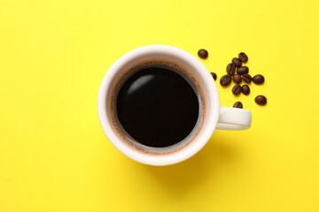 Fresh coffee in cup and roasted beans on yellow background, top view