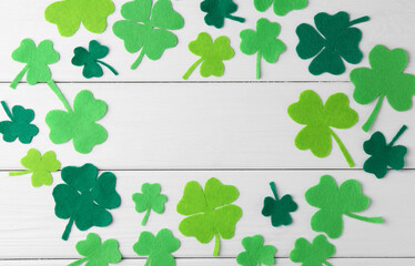 St. Patrick's day. Frame of green decorative clover leaves on white wooden table, flat lay. Space...